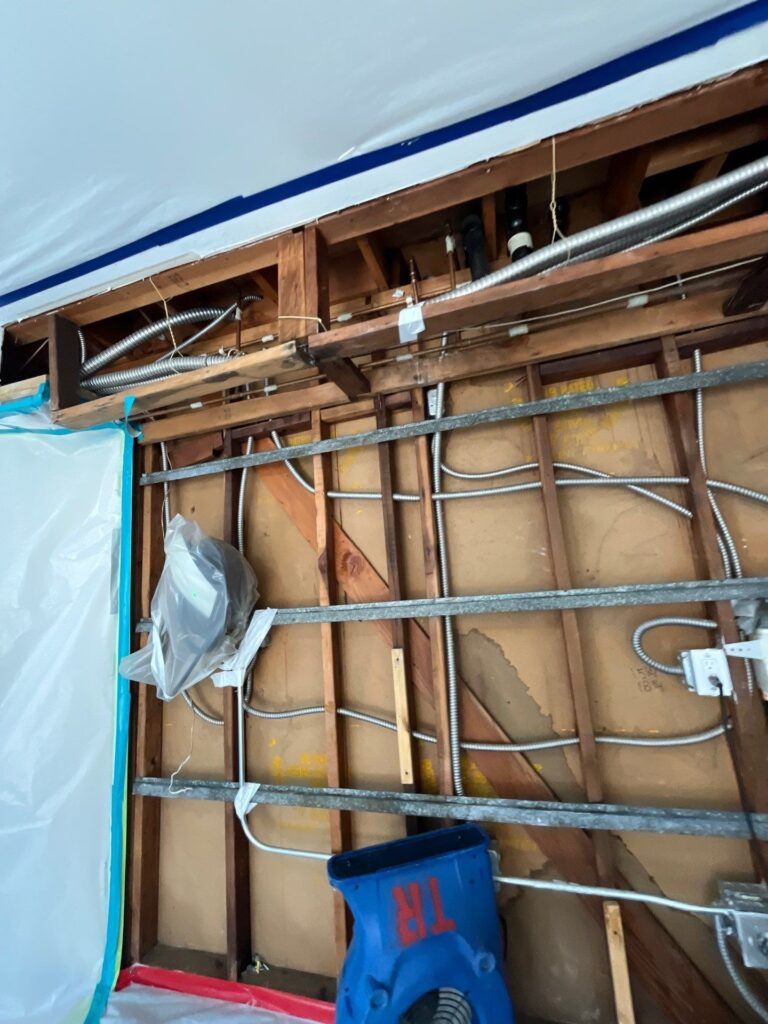 Laundry wall opened to the studs inside plastic containment with an air mover drying the framing