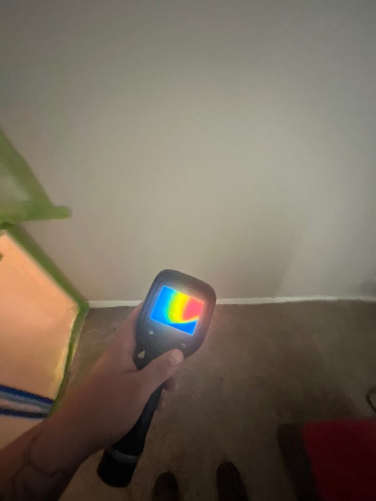 Thermal camera reading along a bedroom wall to find mold behind drywall
