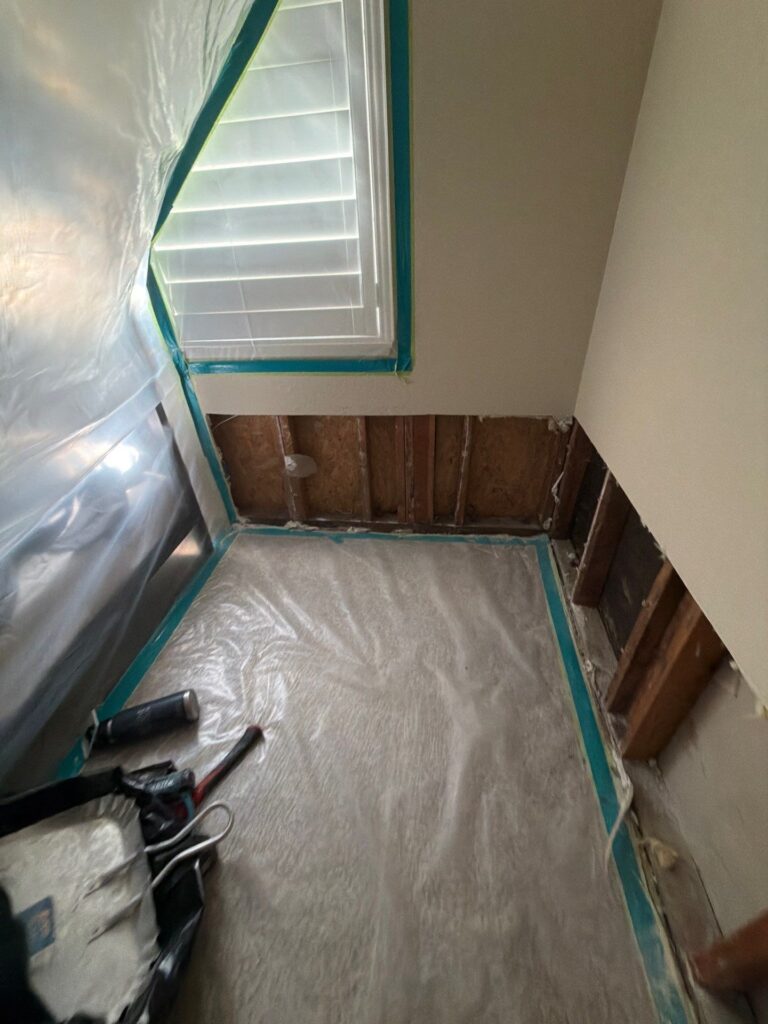 Plastic containment and drywall removed along the bottom of a bedroom wall