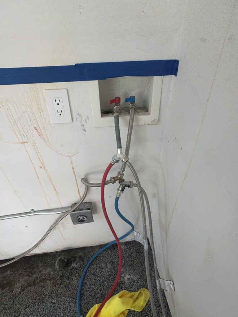 Washer box and supply hoses with drip stains on the wall below from a washing machine leak